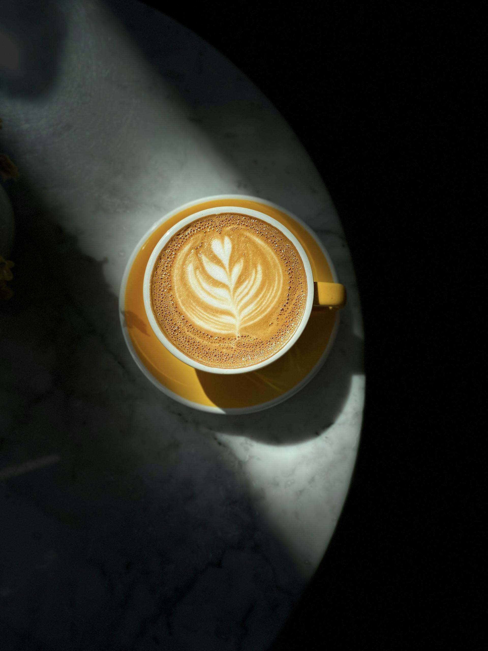 Top view of a beautifully crafted latte with art on a marble table under dramatic lighting.