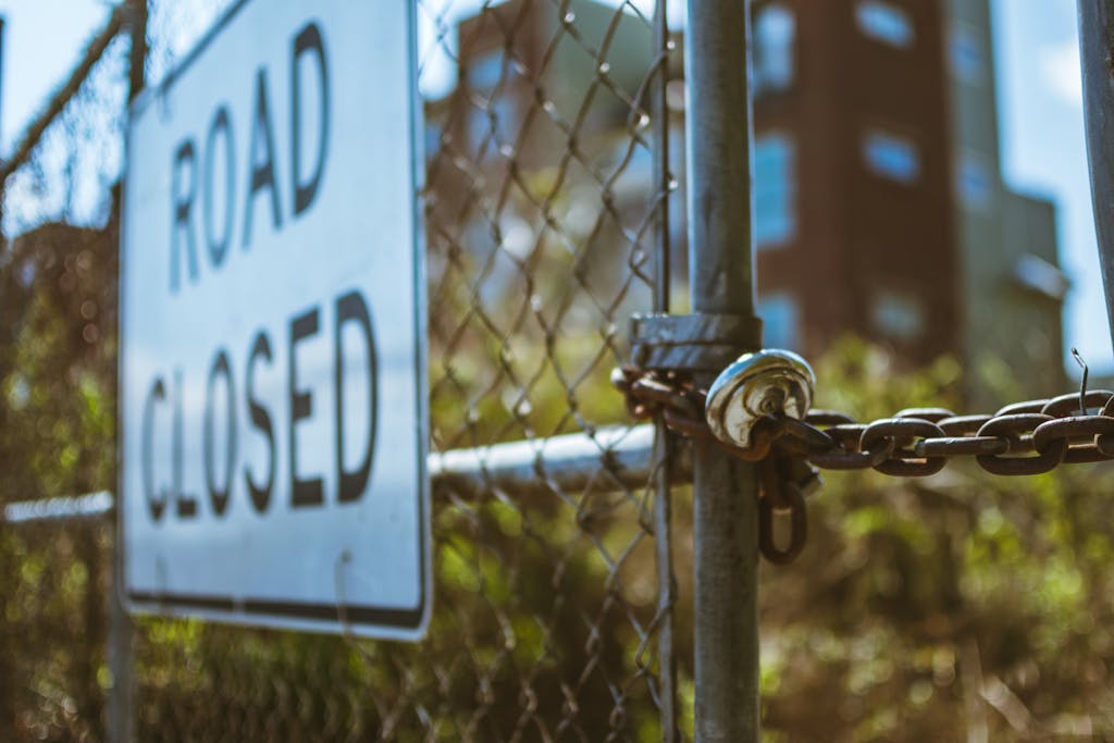 Close-up of a locked chain fence with a road closed sign, symbolizing security.