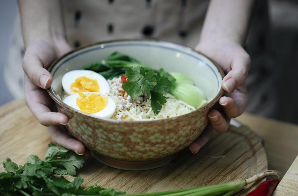 A steaming bowl of homemade ramen with eggs, greens, and noodles in a kitchen setting.