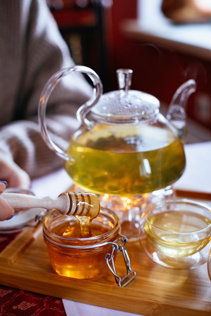 A warm and inviting scene featuring a glass teapot with tea and a jar of honey on a wooden tray.