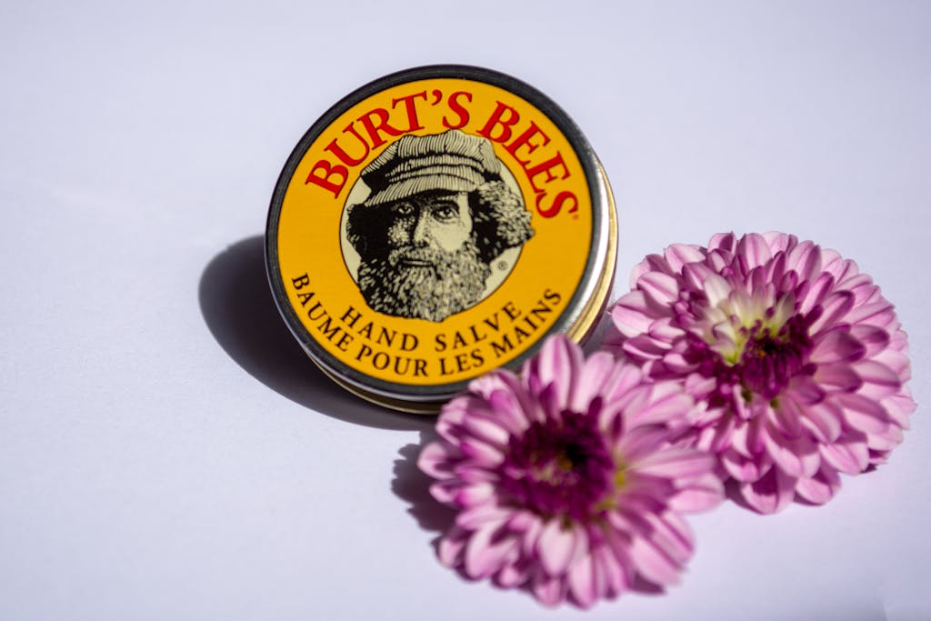 Close-up of Burt's Bees hand salve tin with purple flowers on a white surface.