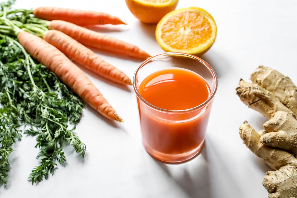 Fresh carrot ginger and orange juice surrounded by ingredients on a white background.