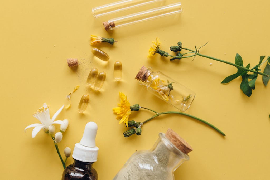 Top view of herbal supplements, flowers, and essential oils for natural wellness on yellow background.