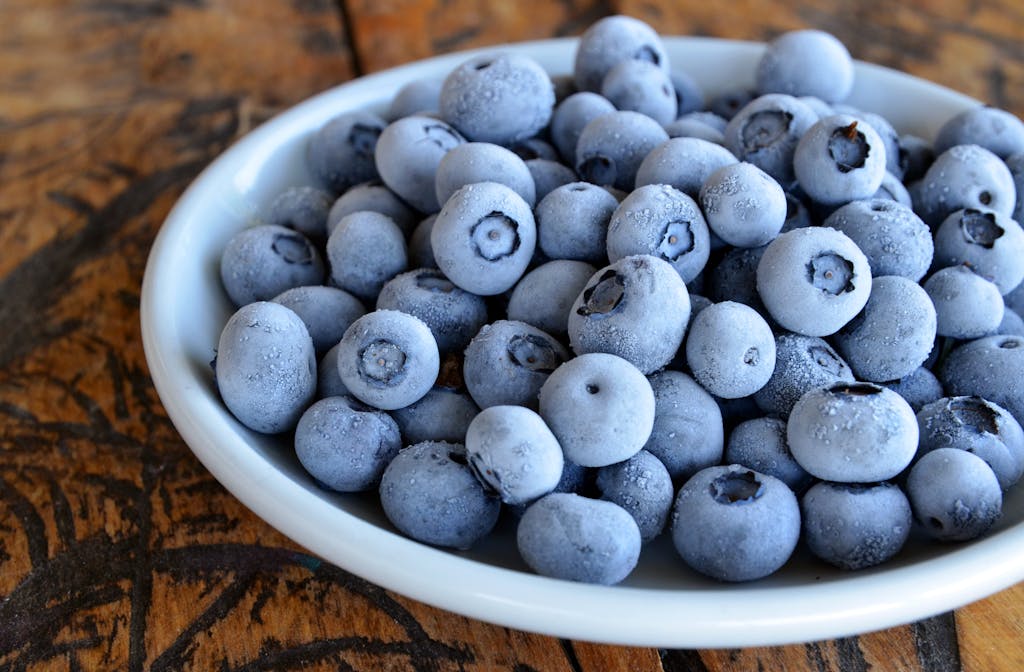 Close-up of frozen blueberries in a white bowl on a rustic wooden table, highlighting texture.