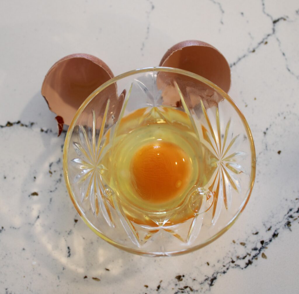 An egg that has been cracked in a small glass bowl. 