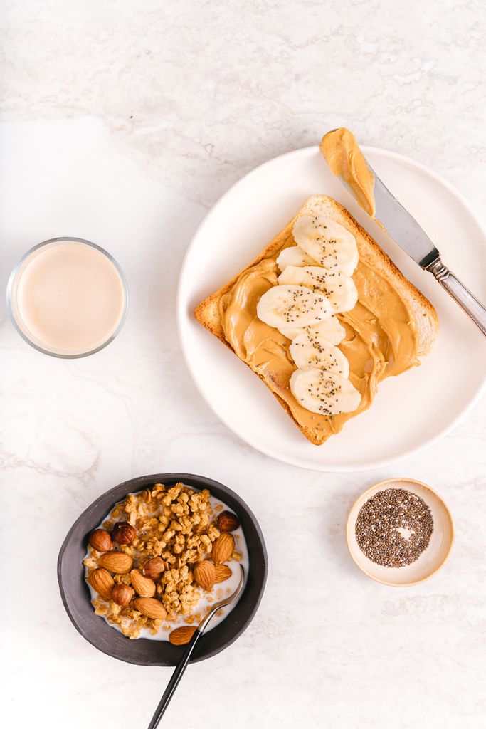 Top-down view of peanut butter banana toast with nuts and chia seeds on marble surface.