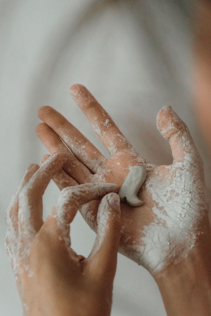 A close-up shot of hands sculpting with clay, dusted in white powder.
