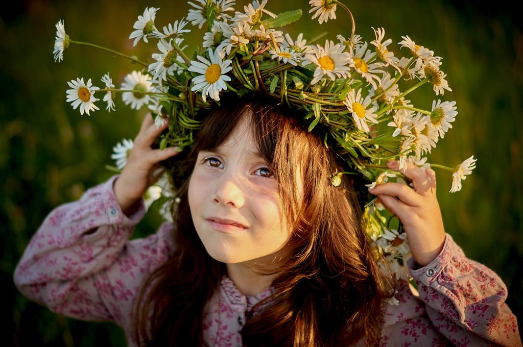 A young girl smiles under a daisy flower wreath, capturing the essence of summer and innocence.