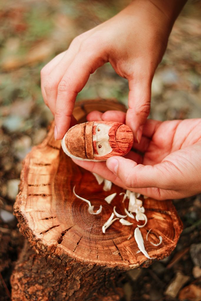 Detailed view of hands crafting a wooden figure on a rustic tree stump outdoors.