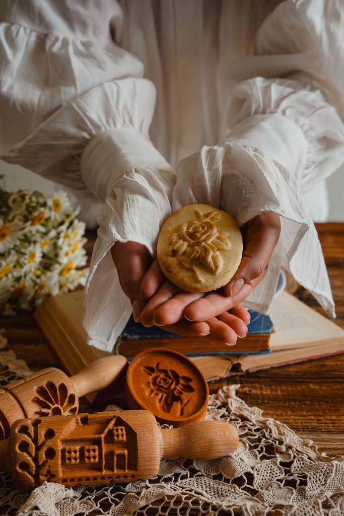 Hands holding a decorative cookie with wooden molds on a rustic table, evoking a traditional baking theme.