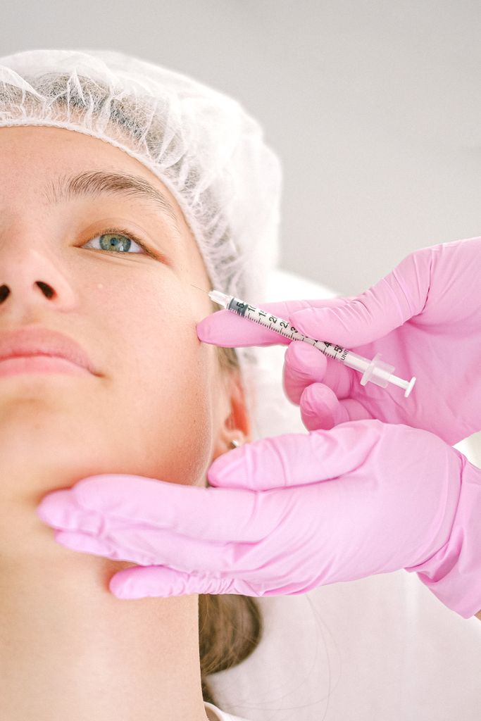 Close-up of a beautician administering facial injection treatment to a woman in a clinical setting.