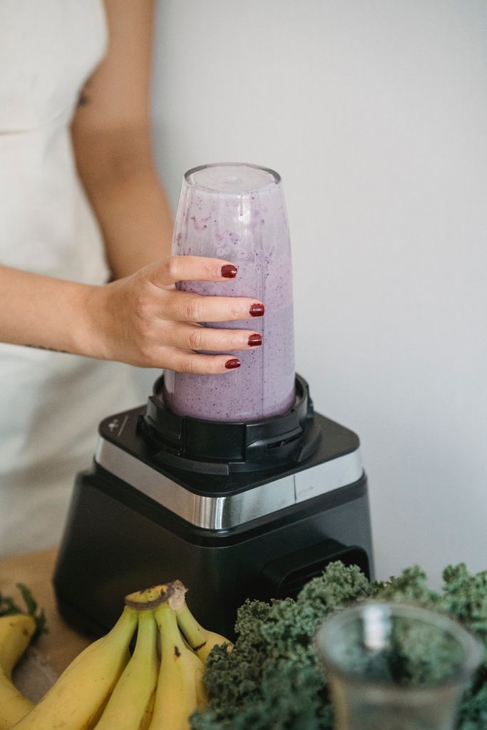 Close-up of a woman blending a nutritious purple smoothie with fresh fruits and greens.