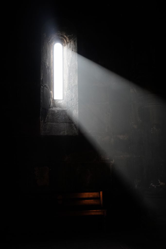A dramatic beam of light streams through a narrow window, illuminating a dark room.